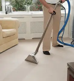Professional carpet cleaner using a hot-water extraction wand and hose machine in a living room in Spokane, WA.