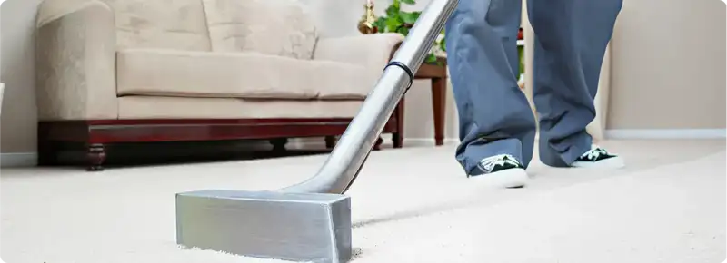 Carpet cleaning technician using a hot-water extraction wand on a light-colored carpet in a living room, Spokane, WA.