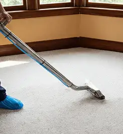 Steam carpet cleaning technician using a hot-water extraction wand on a residential carpet, wearing blue protective shoe covers Spokane, WA.