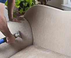 Professional upholstery cleaner deep-cleaning a fabric sofa with a handheld extraction tool and hose in Spokane, WA.